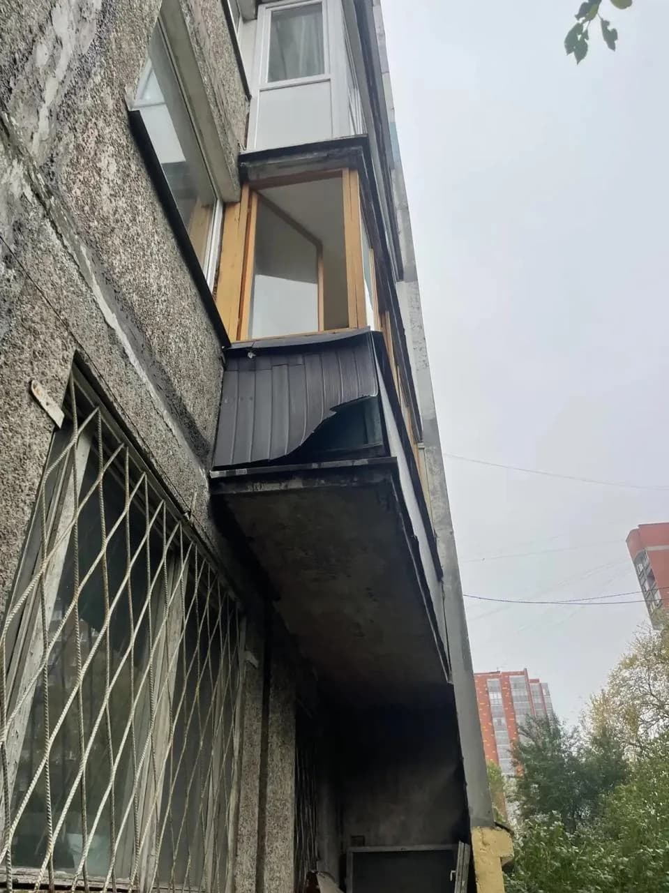 Старое остекление балкона с коричневыми рамами и тёмной обшивкой, боковой вид с улицы