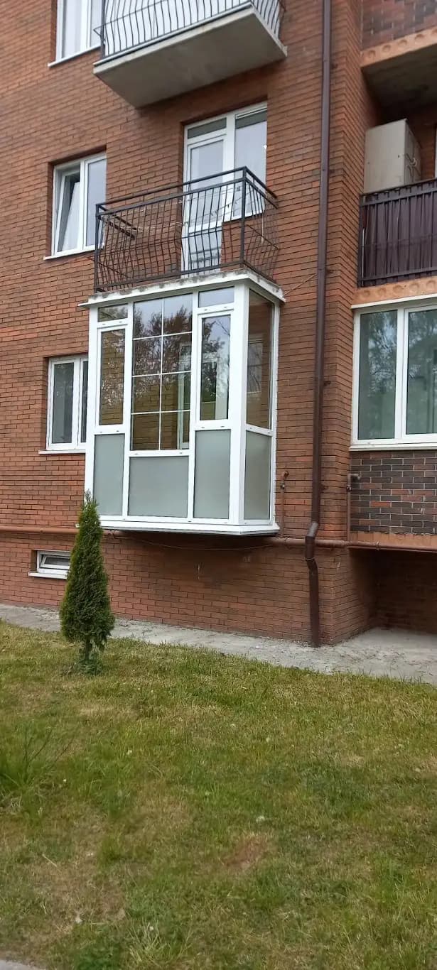Остеклённый балкон на кирпичном фасаде с прозрачными верхними и непрозрачными нижними секциями